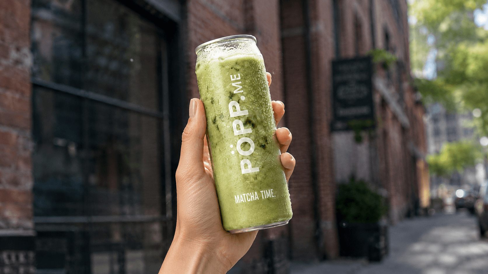 Eine Hand, die eine eiskalte, frisch geschüttelte Matcha Latte Dose präsentiert